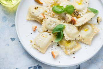 Close-up of italian ravioli served with different types of cheese and fresh basil on a white plate, horizontal shot