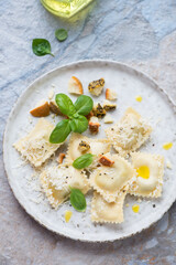 Plate of ravioli with cheese and fresh basil, vertical shot on a beige and blue stone background, elevated view