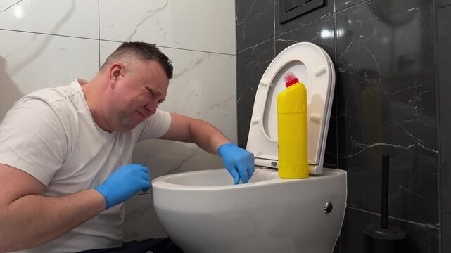 A man struggles to clean a toilet using cleaning liquid. Despite scrubbing, stains remain. He looks frustrated and exhausted with the poor result