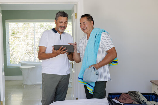 Two senior men smiling while looking at tablet in bedroom, enjoying leisure time