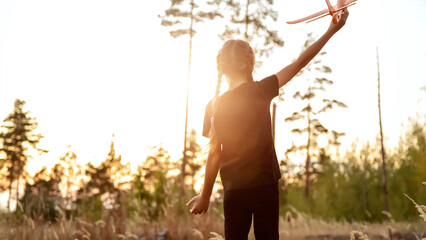 Girl play with toy airplane. Children toy plane in hands of child in summer in park under sun. Concept of child's dream of flying, child runs across field at sunset.