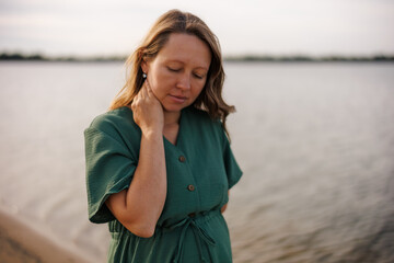 Pregnant girl in green dress walks with dog on lake shore. Owner walks Jack Russell terrier on sea shore. Pet training. Portrait of pregnant woman