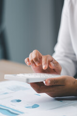 Concept of financial planning and accounting. A businesswoman uses a calculator to analyze reports and charts, calculating budget and investment strategy with focus and precision at office desk.