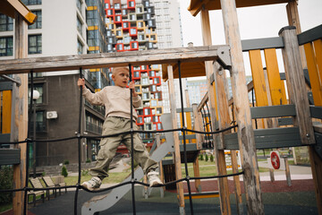 Naklejka premium On a summer day, a boy climbs an alpine grid in a park on a playground. Playground in a public park, entertainment and recreation for children.