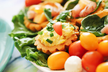 Delicious festive appetizer tarts. Fresh salad and tomato decoration. Homemade savory finger food. Crispy pastry baskets with creamy filling. Colorful vegetables for celebration.
