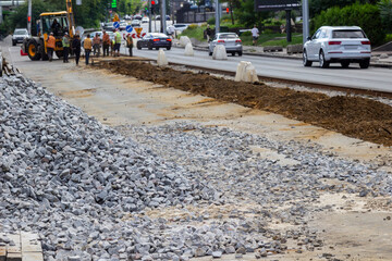  pile of granite gravel. Motor vehicles are driving along the road. Repairmen are repairing tram tracks.