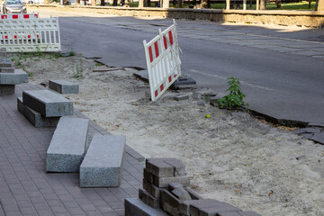 Road repair. Granite curbstone and road bricks at the repair site. Warning barrier on the road