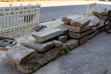 Granite curbstone at the repair site. Warning fence on the road. Repair works