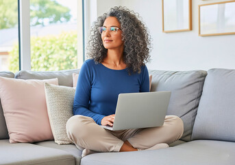 Naklejka premium Reflective Moments of Inspiration: A woman, laptop in lap, sits thoughtfully on a sofa, bathed in natural light, capturing a moment of calm and inspiration while working remotely.