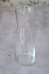 Hand holding an empty transparent glass vase on a table. Minimalist home decor, interior design accessory, and decorative container for flowers or plants.