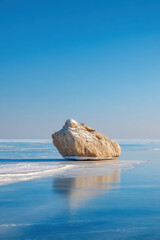 large stone rests majestically on sheet of ice reflecting sunlight under clear sky