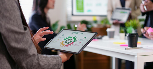 Business presentation on tablet showing circular infographic with team collaborating in modern office, energetic