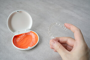 Clear dental aligner in hand and orange case on table. Dental orthodontic mouthpiece.