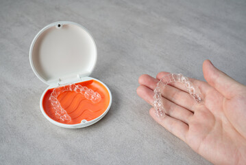 Clear dental aligner in hand and orange case on table. Dental orthodontic mouthpiece.