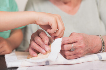 Close-up of child and grandmother sewing together by hand