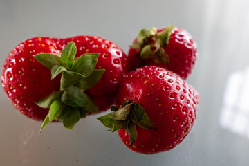 Macro photograph of fresh ripe strawberries with green leaves on a reflective surface. The vibrant red berries emphasize freshness, healthy eating, organic farming, and natural produce.
