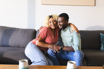 Couple sitting on sofa, embracing and smiling, enjoying quality time together