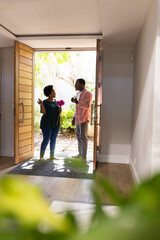 Greeting at doorway, African American friends holding flowers, smiling warmly