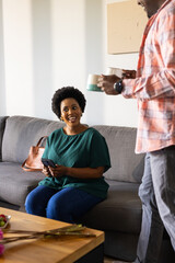 Smiling woman holding smartphone on couch while friend offers coffee mugs