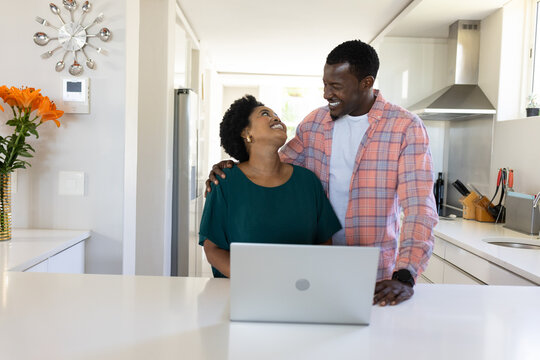 African American couple smiling and using laptop together in modern kitchen
