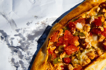 A close-up of a freshly baked Turkish pide, a traditional flatbread, with a savory topping of chicken, tomatoes, peppers, and melted cheese