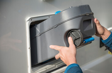 Person removing portable waste tank with handle and wheels from camper van sanitation compartment © C&A