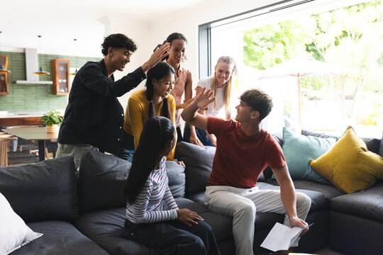 Teenagers high-fiving and celebrating success together in modern living room - Powered by Adobe