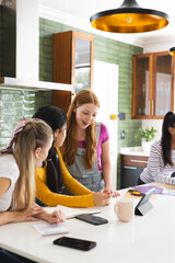 Teen girls collaborating on school project at home, using tablet and notes