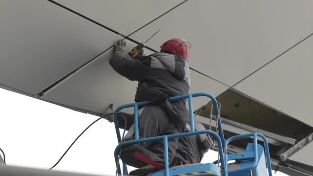 Worker in suspended basket installs cladding tile on modern facade. Careful precise movement shows professionalism and responsibility