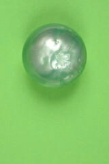 A vertical, top-down studio shot of a single, opalescent sphere with a pearl-like sheen, casting a shadow on a green background