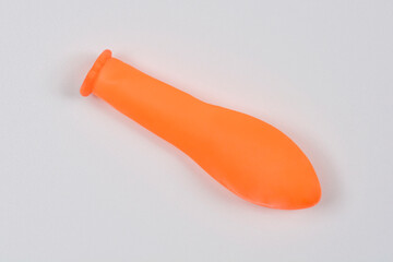 A top-down view of an uninflated, orange rubber balloon lying on a plain white background