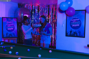 Teen girls celebrating birthday with cake at disco-themed party, smiling joyfully