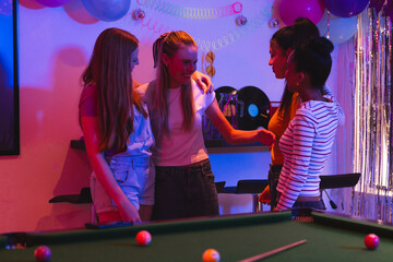 Teen girls celebrating together around pool table, enjoying festive party atmosphere