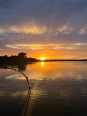 Summer sunset landscape sun setting over Norfolk Broads England uk tranquil water with the beautiful orange yellow blue skies viewed from sailing boat to horizon and trees reeds, clouds reflected 