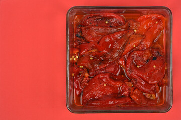 An overhead shot shows roasted red Macedonian peppers in a glass dish on a vibrant red background with plenty of copy space