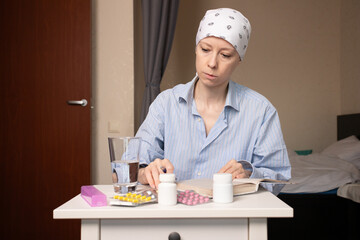 Oncology patient with bald head covered by scarf surrounded by medicine bottles and blister packs,...