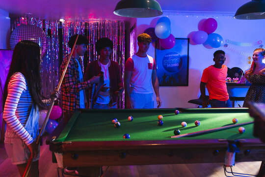 Teenagers playing pool at lively party, enjoying vibrant celebration with friends