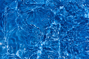 Blue water with ripples on the surface. Defocus blurred transparent blue colored clear calm water surface texture with splashes and bubbles. Water waves with shining pattern texture background.