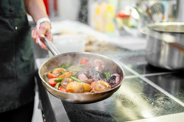 Chef cooking octopus and vegetables in a steaming pan on stovetop. Colorful ingredients, professional kitchen, dynamic food preparation scene