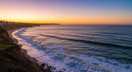 Fototapeta premium Coastal sunset view. Ocean waves crashing at shore, cliffside view. Warm colors of twilight. Distant buildings