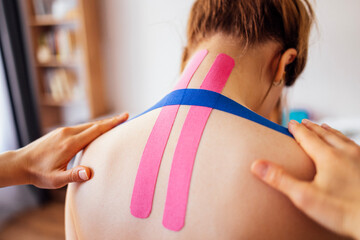 Female athlete receiving kinesiology tape treatment on her back, showcasing colorful tape application, in a bright and inviting therapy room, emphasizing wellness and recovery process