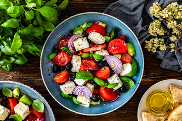 Greek style salad - tomatoes with feta cheese, basil leaves, red onion and black olives on wooden table	