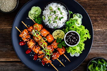 Fried teriyaki salmon skewers with white rice on wooden table