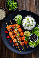 Fried teriyaki salmon skewers with white rice on wooden table