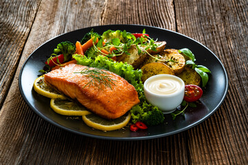 Fried salmon steak with boiled broccoli and mini carrots, fried potatoes and mayonnaise on wooden table	