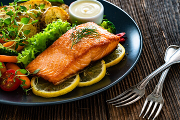 Fried salmon steak with boiled broccoli and mini carrots, fried potatoes and mayonnaise on wooden table	