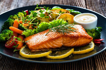 Fried salmon steak with boiled broccoli and mini carrots, fried potatoes and mayonnaise on wooden table	