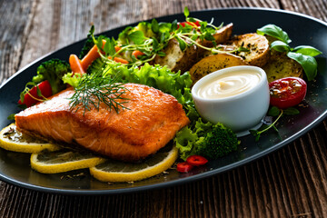 Fried salmon steak with boiled broccoli and mini carrots, fried potatoes and mayonnaise on wooden...