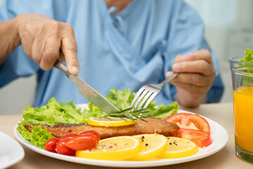 Asian elderly woman patient eating salmon stake and vegetable salad for healthy food in hospital.