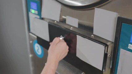 High angle view work woman hands unlocking washer filter drawer with key, ensuring equipment maintenance, promoting hygiene in laundromat with stainless machines under regular service routine